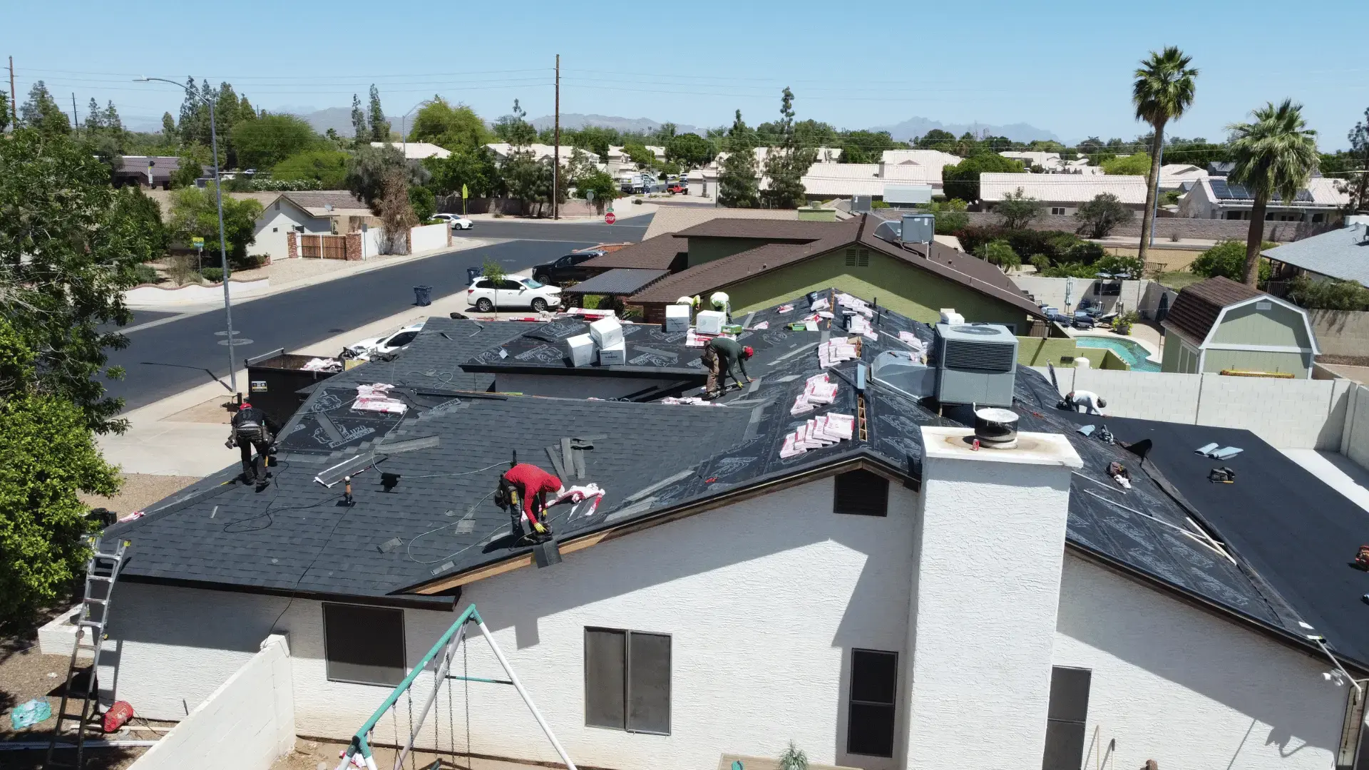 black onyx shingles | Triumph Roofing Roofing crew installs new shingles on a two-story house; workers spread underlayment and materials on a black roof, suburban neighborhood in background